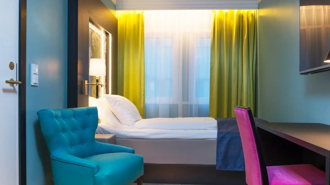 Enkeltseng, gule gardiner, skrivepult, TV og lenestol på Thon Hotel Terminus i Oslo sentrum