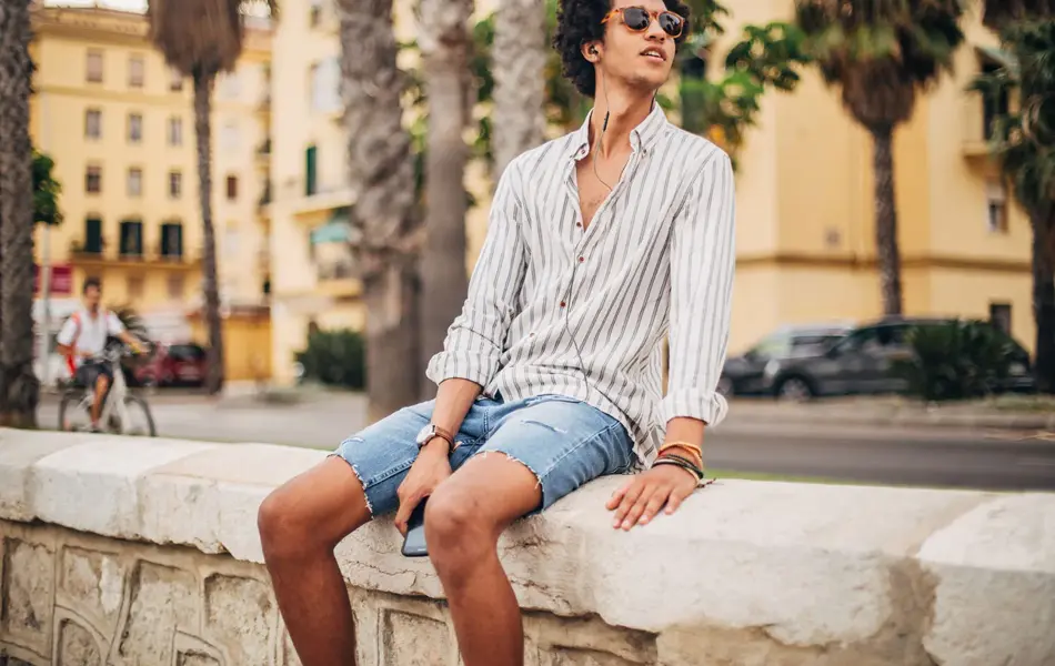 Mann i stripete skjorte sitter på en mur i en by.