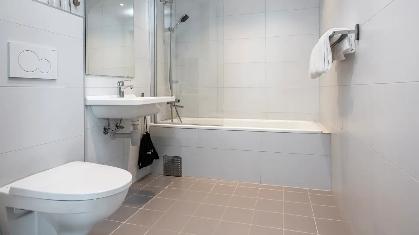 Bad med dusj i badekar, servant, speil og toalett.