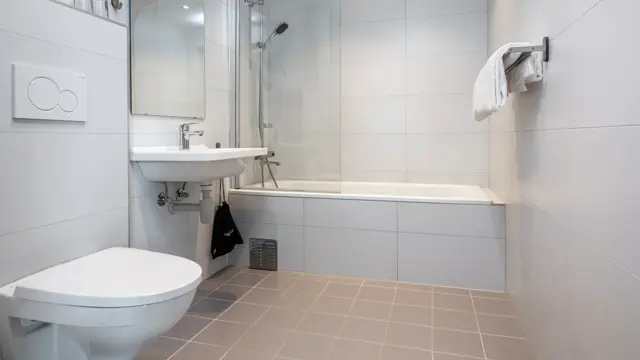 Bad med dusj i badekar, servant, speil og toalett.