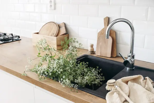 Closeup of kitchen interior. White brick wall, metro tiles, wooden countertops with chopping boards. Cow parsley plants in black sink. Modern scandinavian design, home staging, cleaning concept.