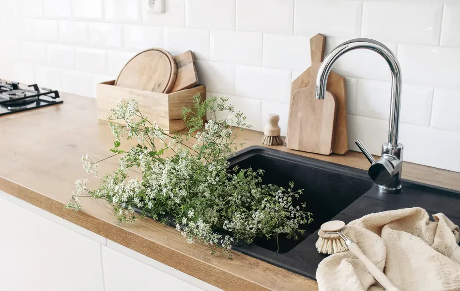 Closeup of kitchen interior. White brick wall, metro tiles, wooden countertops with chopping boards. Cow parsley plants in black sink. Modern scandinavian design, home staging, cleaning concept.
