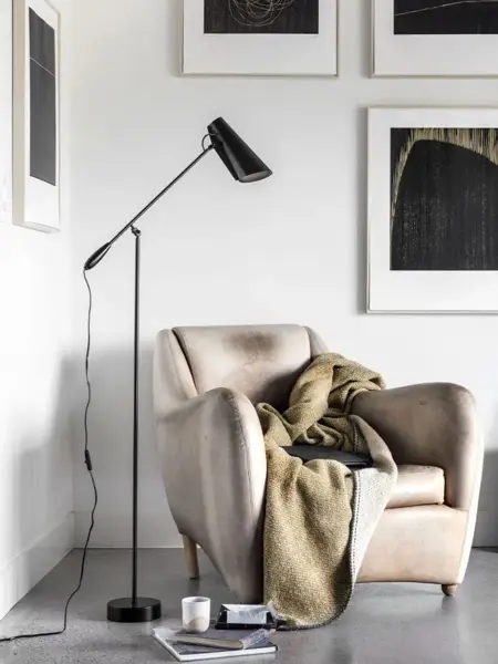 Lenestol med pledd i et hjørne med en sort gulvlampe ved siden av.