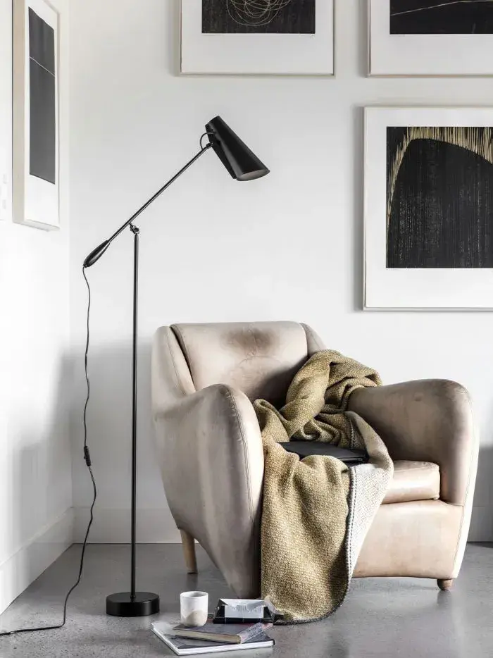 Lenestol med pledd i et hjørne med en sort gulvlampe ved siden av.