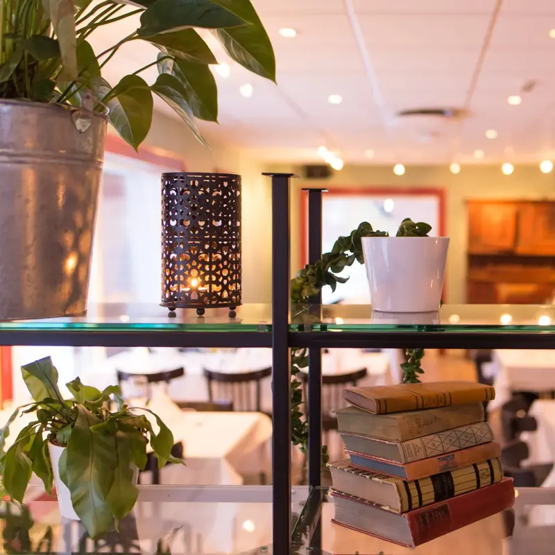 Lykt med lys og bokhylle med plante og bøker med restaurant Jegerstugu Cafe & Bar i bakgrunnen på Thon Hotel Hallingdal