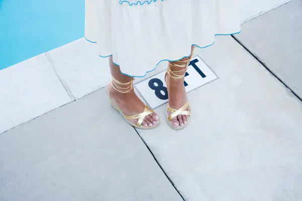 Nærbilde av føtter med gullsandaler stående ved bassengkant 