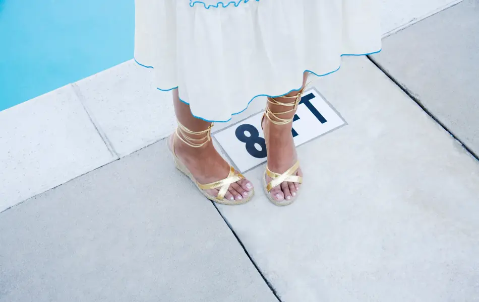 Nærbilde av føtter med gullsandaler stående ved bassengkant 