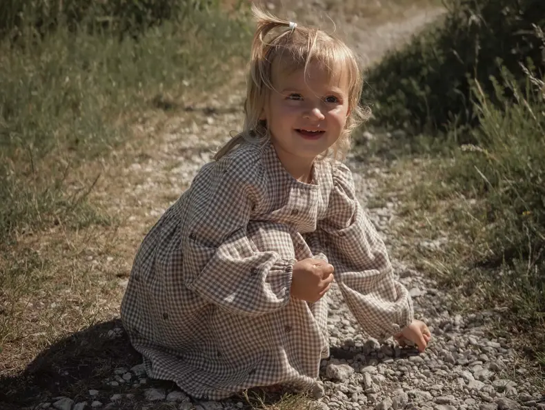 En liten jente i en kjole sitter på huk på en sti.