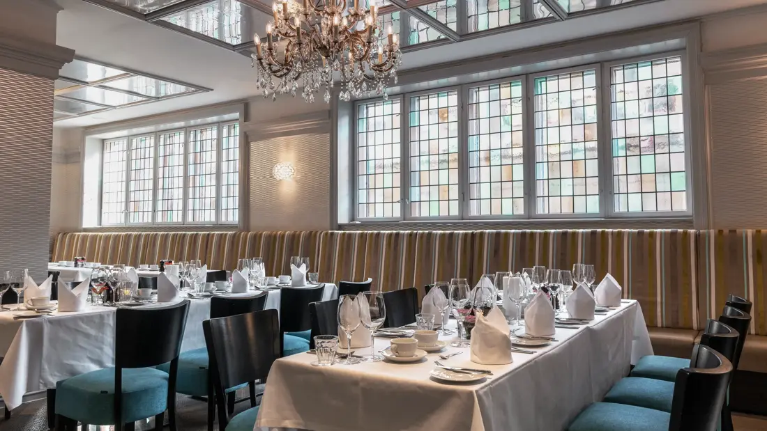 Langbord dekket til selskap i restaurant med hvite duker og servietter og turkise stoler.