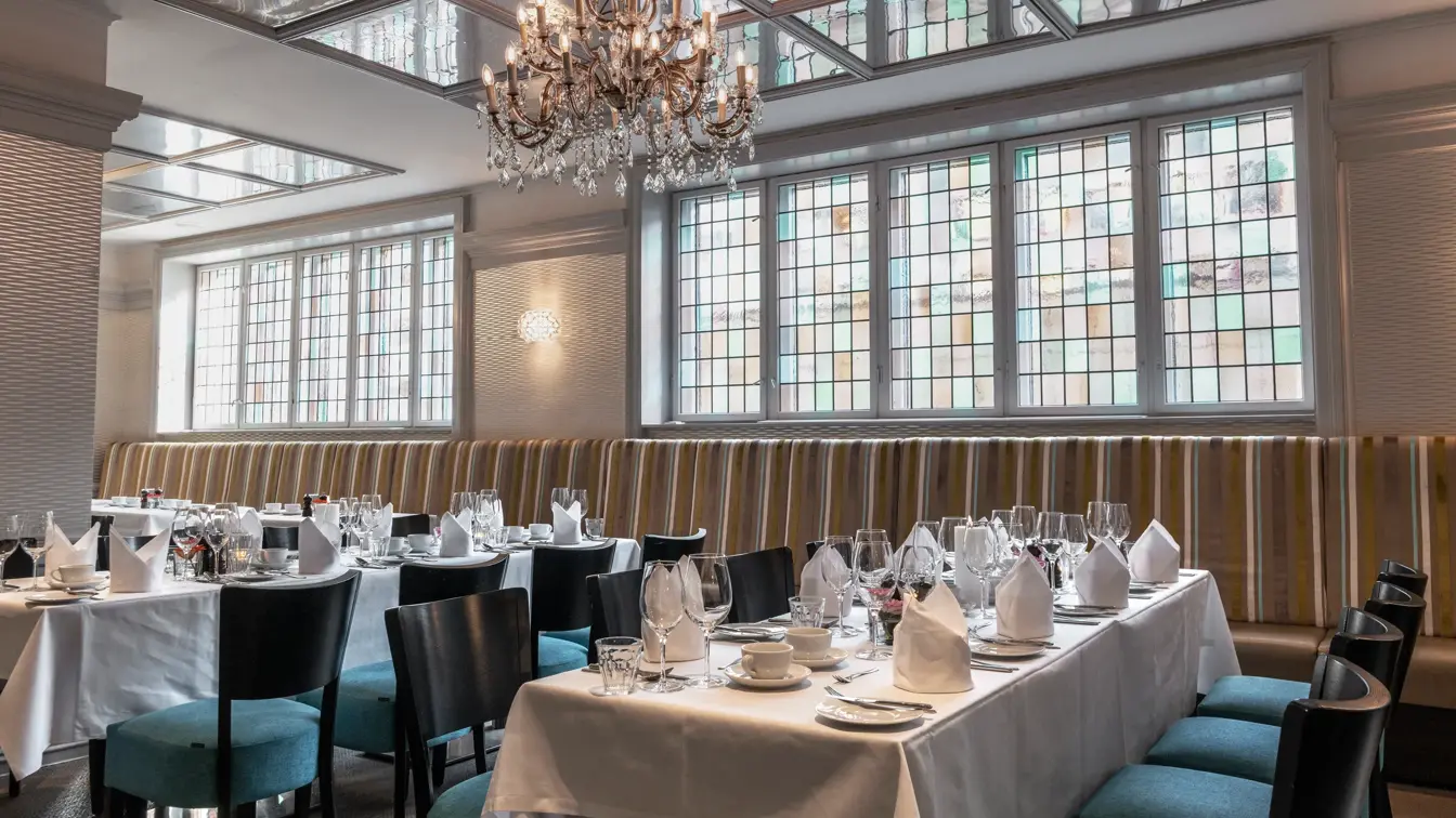 Langbord dekket til selskap i restaurant med hvite duker og servietter og turkise stoler.