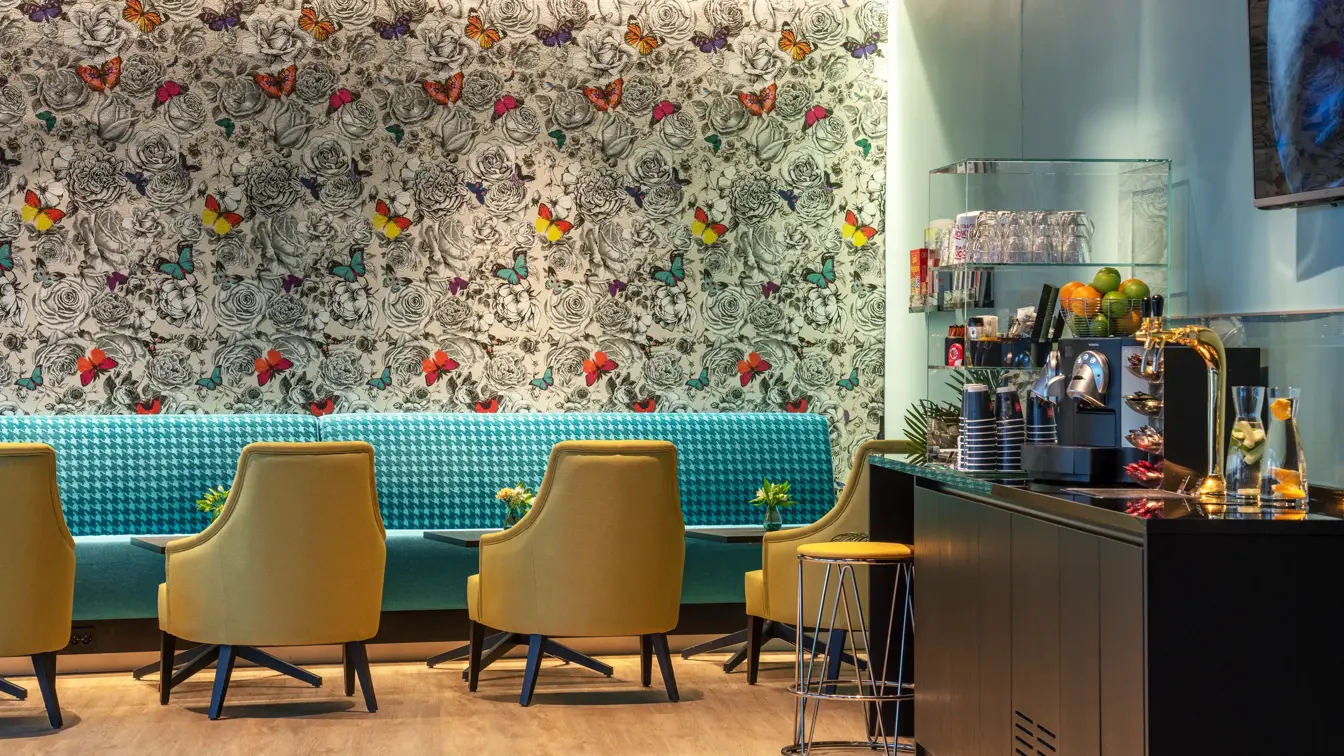 Mønstrete tapet med sommerfugler, turkis sofa og gule stoler. Kaffe og vannstasjon i lobbyen på Thon Hotel Maritim.