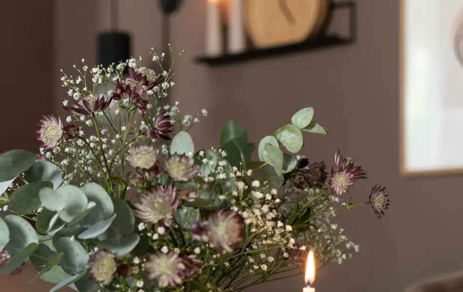 Prikkete vase med en grønn bukett og et brennende lys ved siden av