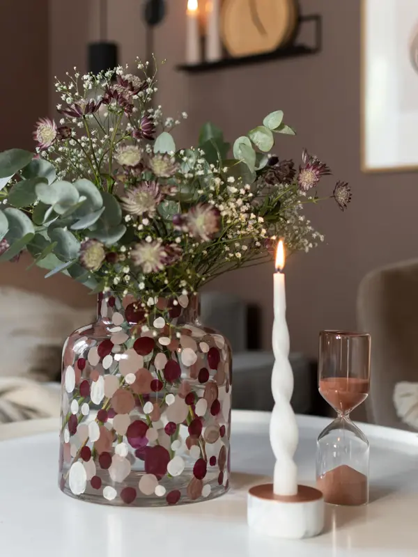 Prikkete vase med en grønn bukett og et brennende lys ved siden av