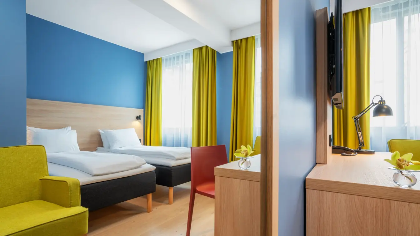 Separate senger, blå vegg, gul stol og gule gardiner på standard rom twin på Thon Hotel Astoria