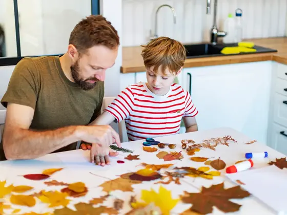 Far og sønn limer høstblader på papir. Foto.