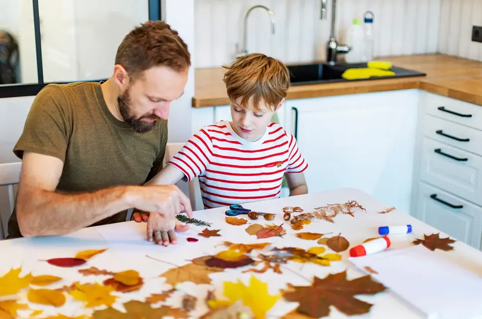 Far og sønn limer høstblader på papir. Foto.
