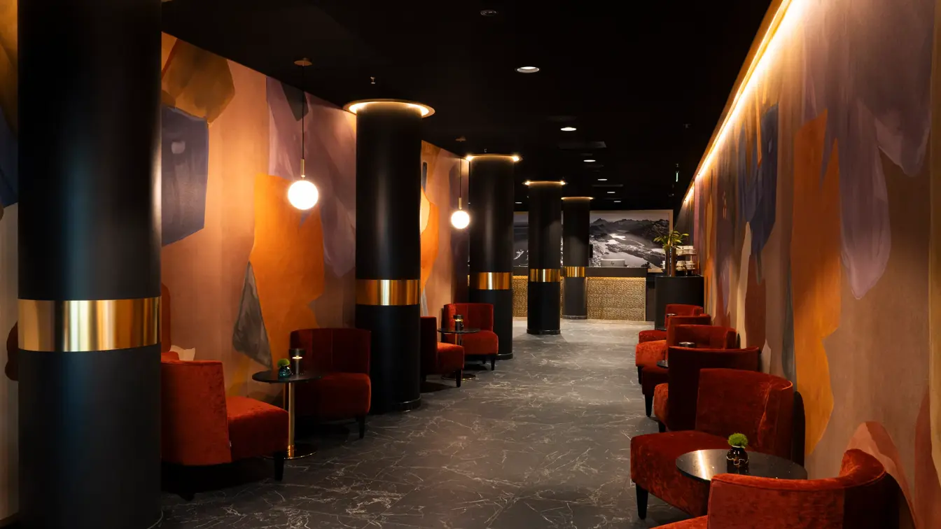 Lobbyområde med sitteplasser og småbord, dempet belysning, røde velour stoler og resepsjonsdisk i enden.
