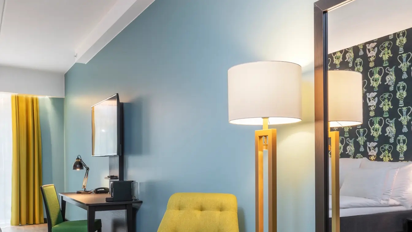 Sittegruppe med gule stoler, speil, turkis vegg, skrivebord og grønn stol i junior suite på Thon Hotel Linne