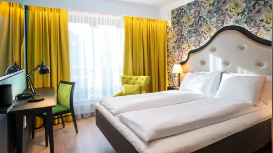 Blomstret tapet og dobbeltseng i dobbeltrom, gule gardiner, tv og arbeidsplass på Thon Hotel Cecil i Oslo sentrum