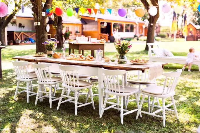 Table set for a garden party or celebration outside. Flowers and sweet and savoury snacks on the decorated table in the garden.
