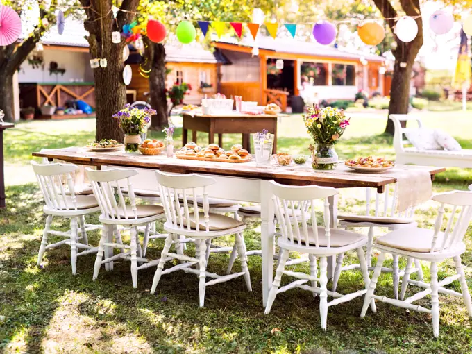 Table set for a garden party or celebration outside. Flowers and sweet and savoury snacks on the decorated table in the garden.