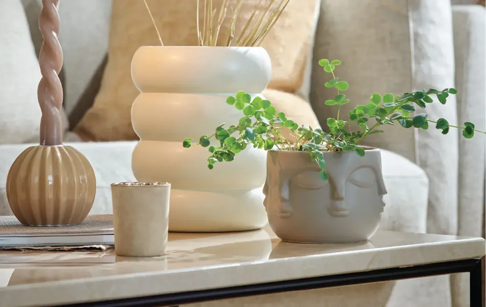 Lys sofa og et bord dekket med en vase med strå, grønn plante og tent lys