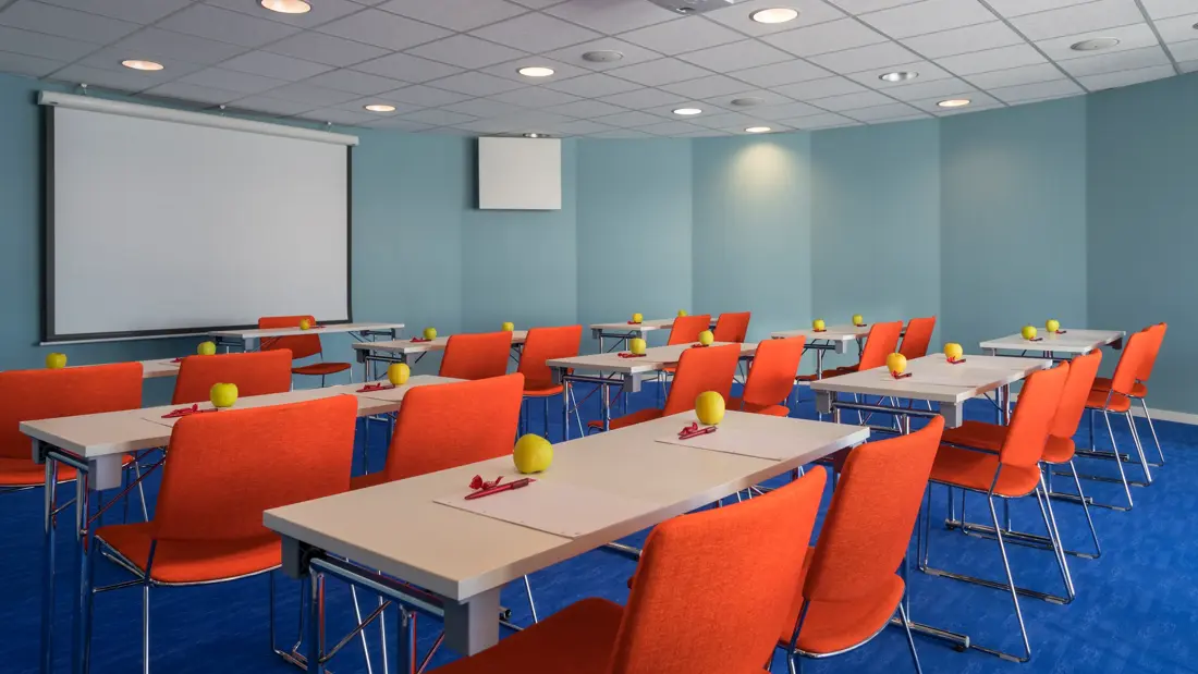 Fargerikt møterom i kurs- og konferanseavdelingen på Thon Hotel Kautokeino. Turkise vegger, blått teppe og oransje stoler. Stor lerret som kan brukes til ulike fremvisninger.