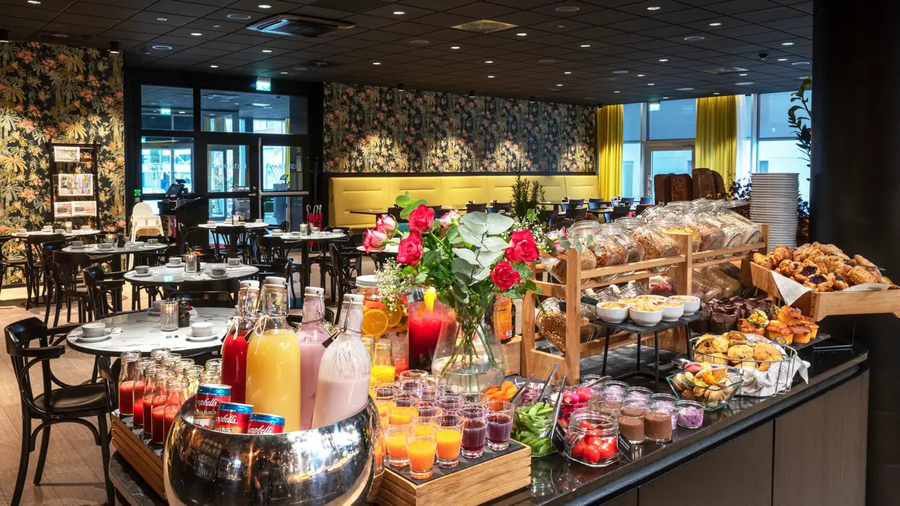 Frokostbuffet, frokostsal med runde spisebord, tapetvegg med blomster, vindu, gule gardiner. 