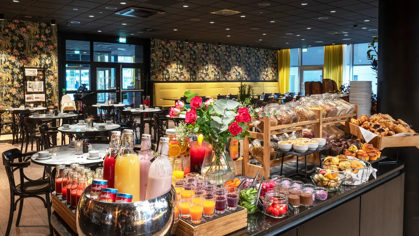 Frokostbuffet, frokostsal med runde spisebord, tapetvegg med blomster, vindu, gule gardiner. 