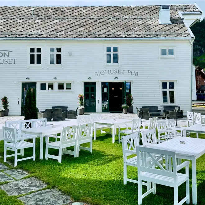 Hvit bygning med hvite utemøbler i hage foran bygningen. 