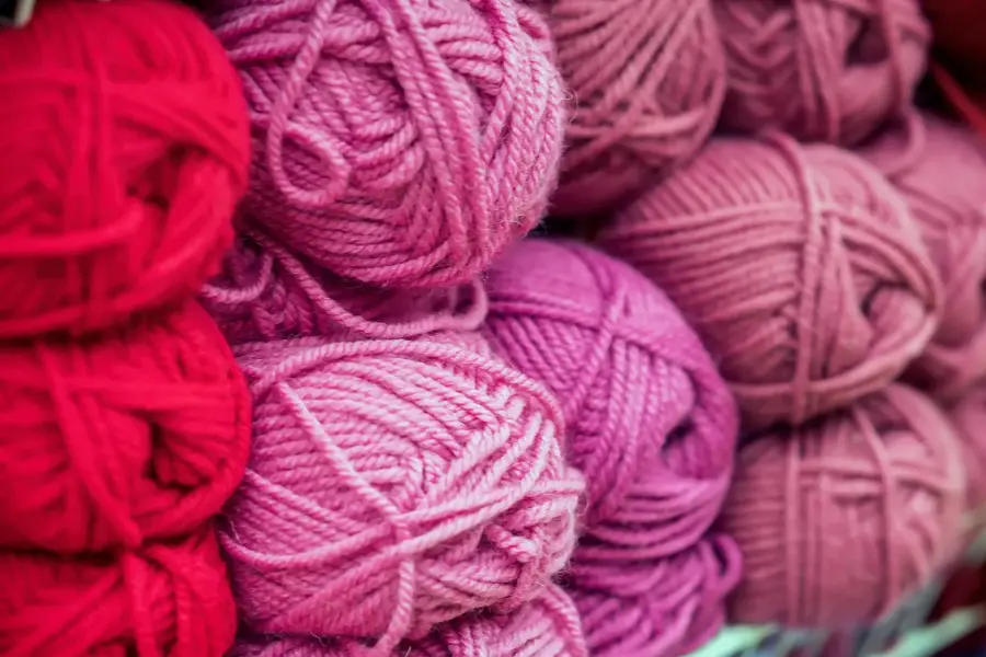 Variegated pile of knitting yarn for knitting in shades of purple, pink, violet. Store of goods for creativity and needlework. Colored multicolored yarn for knitting. Store shelves for craftsmen