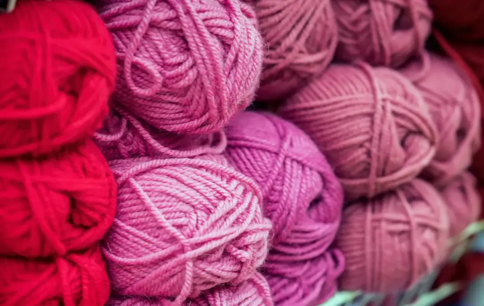 Variegated pile of knitting yarn for knitting in shades of purple, pink, violet. Store of goods for creativity and needlework. Colored multicolored yarn for knitting. Store shelves for craftsmen