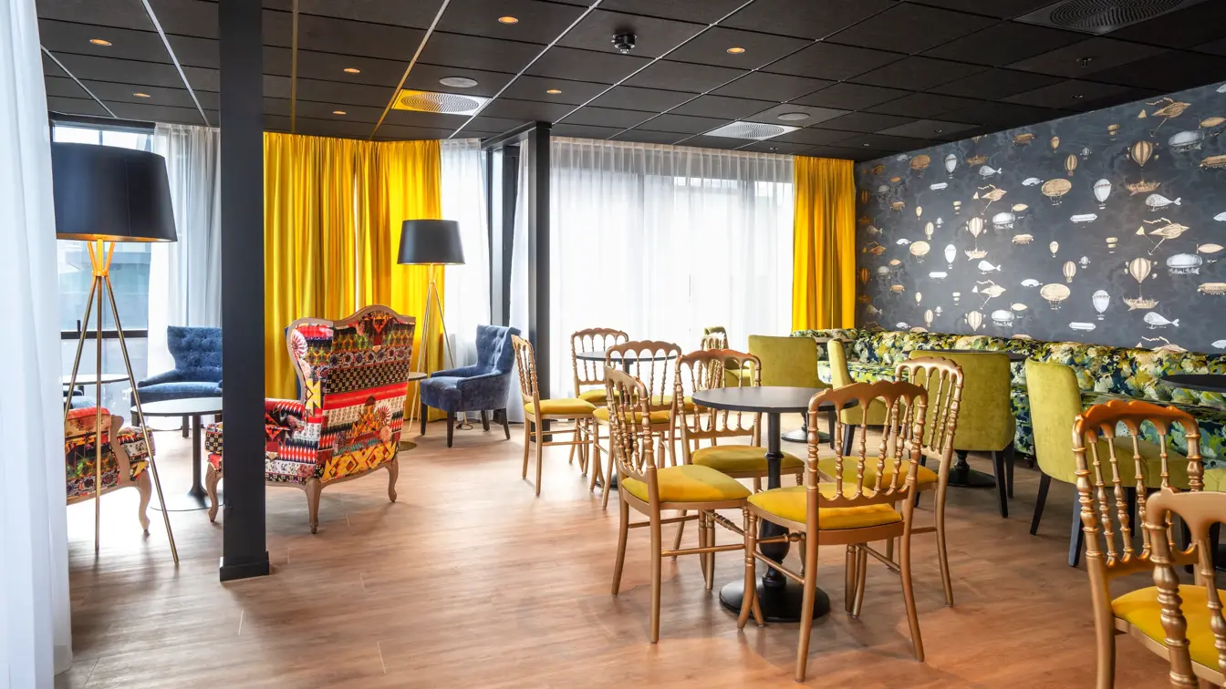 Gule stoler, sorte runde bord, fargerike møbler og gule gardiner i lounge på Thon Hotel Cecil