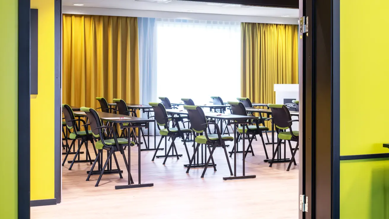 Konferanserom, klasseromoppsett, 1m avstand, grønne stoler, gulv vegg, gule gardiner.