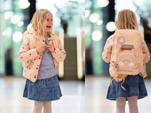 Jente med ytterjakke, olaskjørt, topp og skolesekk smiler og ser til siden. jente med ryggen mot kamera med lysegul skolesekk.