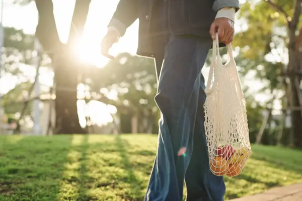 Et bilde av noen som går ute med et handlenett med frukt i.