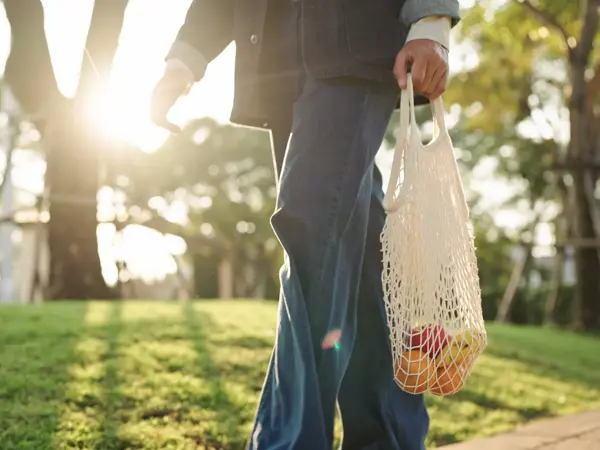 Et bilde av noen som går ute med et handlenett med frukt i.