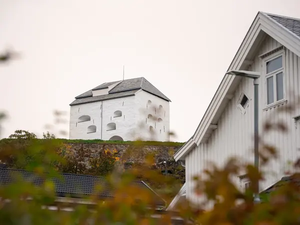 Hvit mursteinsbygning på en bakketopp i overskyet vær