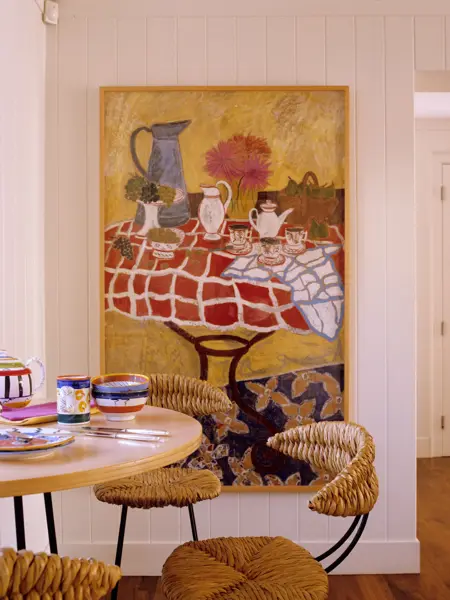 Utsnitt av kjøkken med spisebord dekket på med fargerik keramikk, og fargerikt maleri i bakgrunnen 