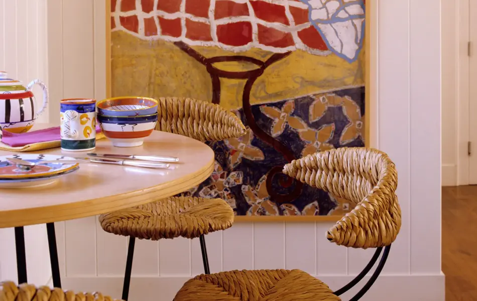 Utsnitt av kjøkken med spisebord dekket på med fargerik keramikk, og fargerikt maleri i bakgrunnen 
