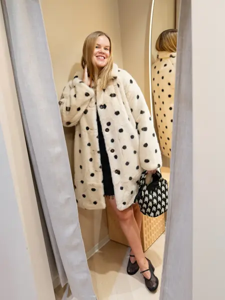 Dame med sort kjole, kort hvit kåpe med sorte prikker, hvit og sort mønstret veske og sorte sko.