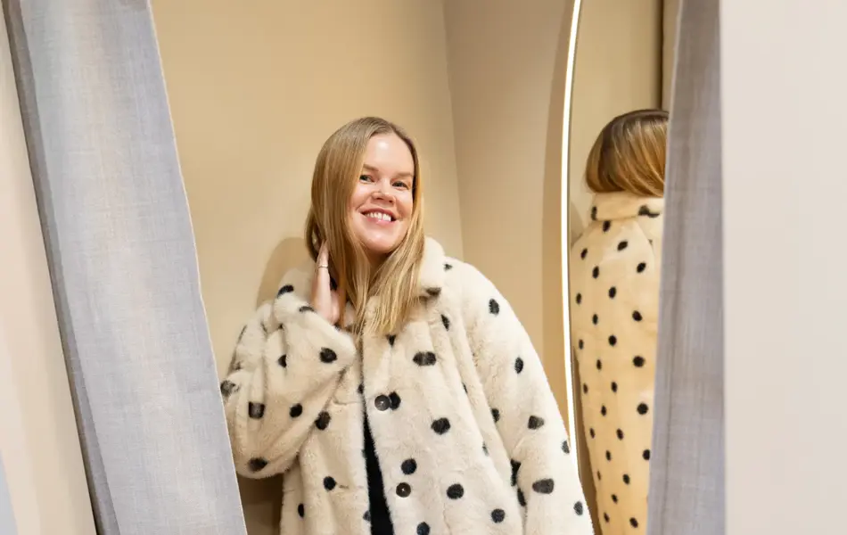 Dame med sort kjole, kort hvit kåpe med sorte prikker, hvit og sort mønstret veske og sorte sko.