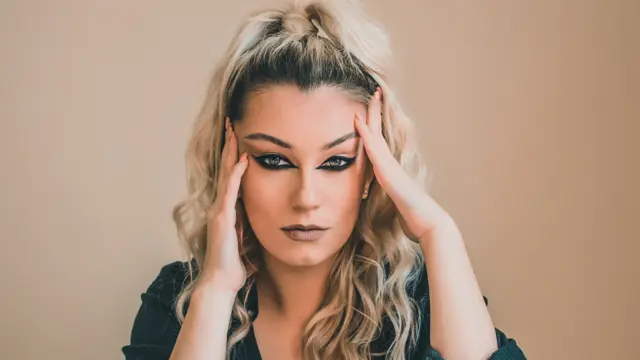 Kvinne med oppsatt hår og reversed cat eye-sminke som ser i kamera