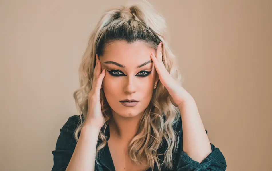 Kvinne med oppsatt hår og reversed cat eye-sminke som ser i kamera