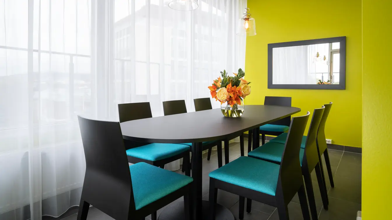 Gule vegger, langt spisebord med 8 stoler, svart gulv, vindu fra gulv til tak, Speil på vegg. 