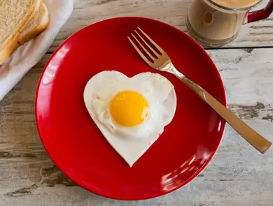 herzförmiges Spiegelei auf rotem Teller, Toast, Kaffee, Gabel, Frühstück, Holztisch, Studio