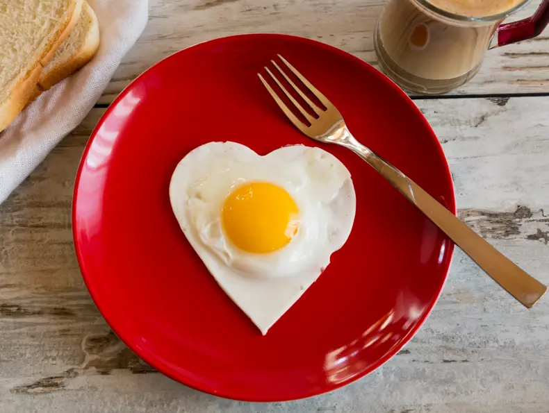 herzförmiges Spiegelei auf rotem Teller, Toast, Kaffee, Gabel, Frühstück, Holztisch, Studio