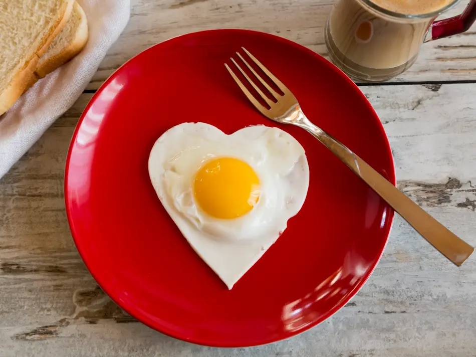 herzförmiges Spiegelei auf rotem Teller, Toast, Kaffee, Gabel, Frühstück, Holztisch, Studio