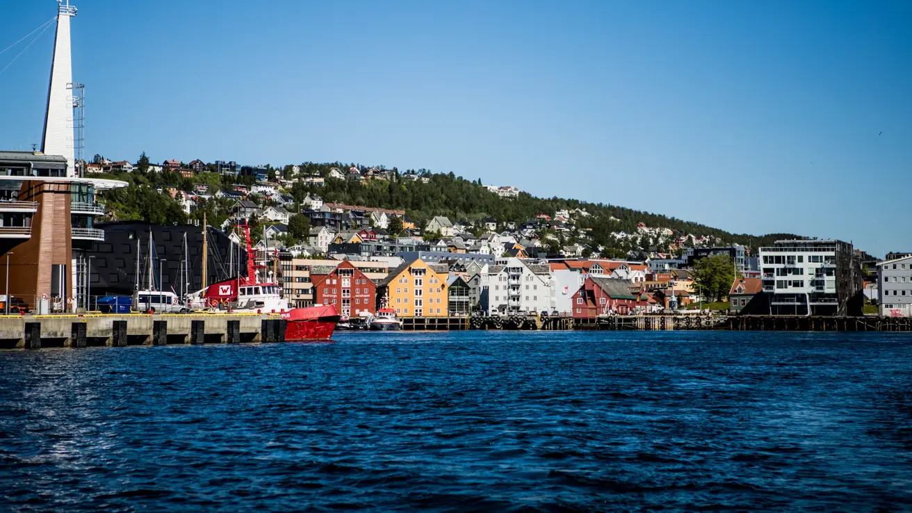Eldre trebygg i sterke farger, som huser bl.a. Polarmuseet, langs vannet i Tromsø.