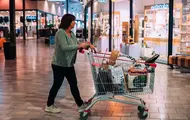 Bildet er fra kjøpesenteret Charlottenbergs Shoppingcenter og viser en dame i grønn strikkejakke med en handlekurv full av ulike bæreposer.